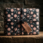 Luxury celestial holiday gift wrap with rose gold stars, leather bow, and Noel tag by Wrapped Studios.