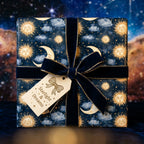 Luxury celestial wrapping paper with gold sun and moon patterns and a navy velvet bow, by Wrapped Studios.