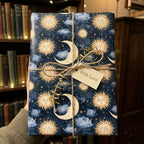 Celestial wrapping paper with vintage sun and moon designs on a gift tied with twine, by Wrapped Studios.