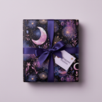 Square gift wrapped in celestial-themed birthday wrapping paper with a dark purple ribbon and tag.