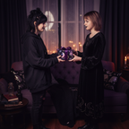 Two women exchanging a gift wrapped in dark floral wrapping paper with a purple ribbon.