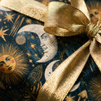 Celestial wrapping paper with vintage sun and moon patterns and a metallic gold bow by Wrapped Studios.