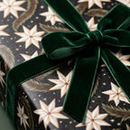 Luxury Christmas wrapping paper with cream stars and a green velvet bow by Wrapped Studios.