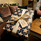 Navy celestial star wrapping paper with cream ribbon and "With Love" gift tag by Wrapped Studios.