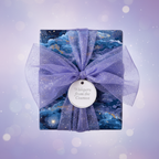 Elegant gift wrapped in blue starry night wrapping paper with a sparkly lavender bow.