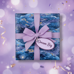 Square gift box in blue celestial wrapping paper with lavender ribbon bow and "Dream Big" tag.