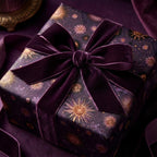 Luxury purple celestial wrapping paper with gold sunbursts and a velvet bow by Wrapped Studios.