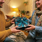 Couple holding a gift in celestial wrapping paper with teal ribbon. Luxury holiday gift wrap by Wrapped Studios.