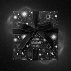 Black celestial wrapping paper with a ribbon and "A Little Starlight For You" tag.