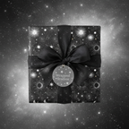 Black square gift wrapped in celestial star and moon patterned wrapping paper, tied with satin ribbon.