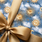 Celestial wrapping paper featuring golden suns and clouds, tied with a gold satin bow by Wrapped Studios.