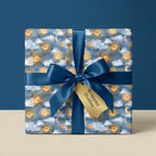 Celestial wrapping paper with gold suns and moons, tied with a blue satin bow by Wrapped Studios.