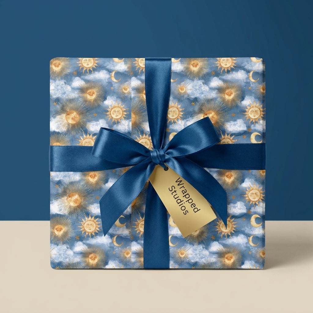 Celestial wrapping paper with gold suns and moons, tied with a blue satin bow by Wrapped Studios.