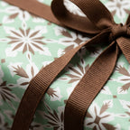 Sage green snowflake Christmas wrapping paper with a brown ribbon by Wrapped Studios.