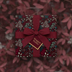 Burgundy floral wrapping paper on a square gift box with a ribbon bow and tag.