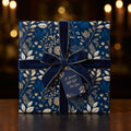 Navy blue floral wrapping paper with gold accents, velvet ribbon, and gift tag for a special gift.
