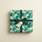 Square gift wrapped in green and white floral wrapping paper, tied with a dark green ribbon and bow.