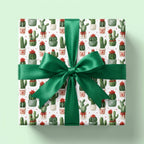 Cactus Christmas wrapping paper by Wrapped Studios on a gift box with a large emerald green satin bow.