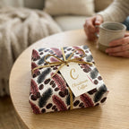 Cozy coffee bean and pine Christmas wrapping paper with a gold bow and tag by Wrapped Studios.