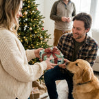 Dog Christmas wrapping paper by Wrapped Studios on a gift exchanged by a couple next to their golden retriever.