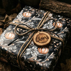 Dark floral wrapping paper with pumpkins tied with twine and "Cheers" wooden tag, perfect for fall.