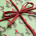 Whimsical frog Christmas wrapping paper featuring frogs in Santa hats with a red bow, by Wrapped Studios.