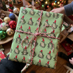 Hands holding a gift in Christmas frog wrapping paper by Wrapped Studios, tied with festive red and white twine.