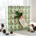 Whimsical frog Christmas wrapping paper by Wrapped Studios, styled on a gift box with twine and holly.