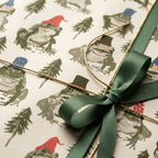 Whimsical frog Christmas wrapping paper with a green satin bow, designed by Wrapped Studios.