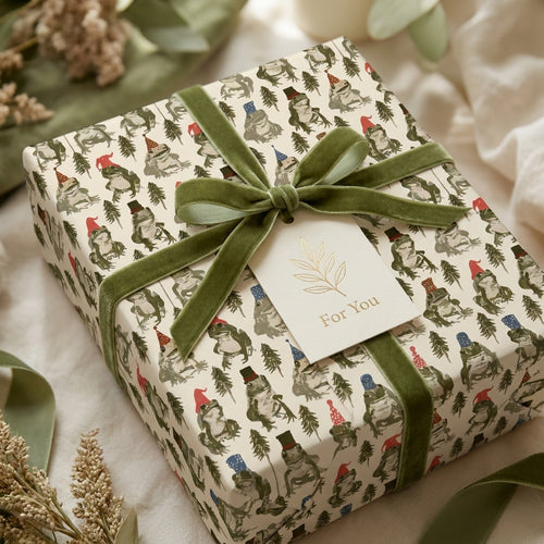 Whimsical frog Christmas wrapping paper with olive velvet ribbon on a gift box by Wrapped Studios.