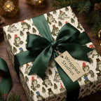 Whimsical frog Christmas wrapping paper with a green satin bow and Wrapped Studios tag.