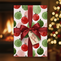 Christmas gift wrapped in festive red and green watercolor ornament paper with a dark red satin bow and "Merry Christmas" tag, by a fireplace.
