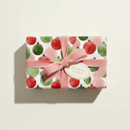 Christmas wrapping paper with red and green ornament pattern, tied with a pink velvet ribbon and "Wrapped Studios" gift tag.