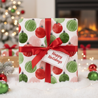 Christmas wrapping paper with red and green ornament pattern, tied with a red ribbon and "Happy Holidays" tag, on faux snow.