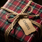 Red plaid Christmas wrapping paper with rustic twine bow and Cheers tag by Wrapped Studios.