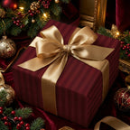 Burgundy striped Christmas gift wrap with gold ribbon and bow on a velvet surface with festive ornaments.