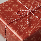 Close-up of a gift wrapped in red Christmas wrapping paper with a white snowflake pattern and a red and white string bow.