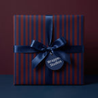 Elegant square gift box wrapped in navy and burgundy striped wrapping paper with a satin navy bow.