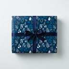 Navy blue floral wrapping paper on a square gift box tied with a dark blue satin ribbon.
