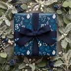 Navy floral wrapping paper with matching ribbon on a square gift box, surrounded by winter foliage.