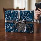 Dark blue gift box wrapped in modern floral wrapping paper with a silver ribbon and a "Cheers to you!" tag.