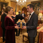 Woman exchanges a luxury wrapped gift with gold ribbon at a formal holiday party.