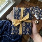 Elegant navy gift wrapped in gold floral wrapping paper with a gold ribbon and bow.