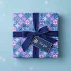Square gift wrapped in blue snowflake Christmas wrapping paper with a velvet ribbon and "For You" tag.