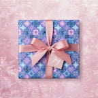 Blue and lavender snowflake Christmas gift wrap with pink ribbon and a "Joy" tag.