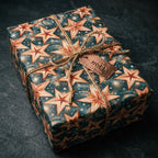 Celestial Christmas wrapping paper with copper stars on navy, tied with twine by Wrapped Studios.
