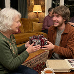 Woman gives floral-wrapped birthday gift with velvet ribbon to smiling man.