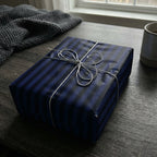 Modern gift wrapped in navy striped wrapping paper with silver string on a wooden table.