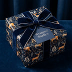 Wrapped Studios luxury gift wrap: dark floral paper with reindeer, tied with a navy velvet ribbon.
