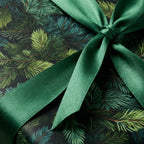 Close-up of a gift wrapped in elegant evergreen tree print Christmas wrapping paper and tied with a satin green ribbon.